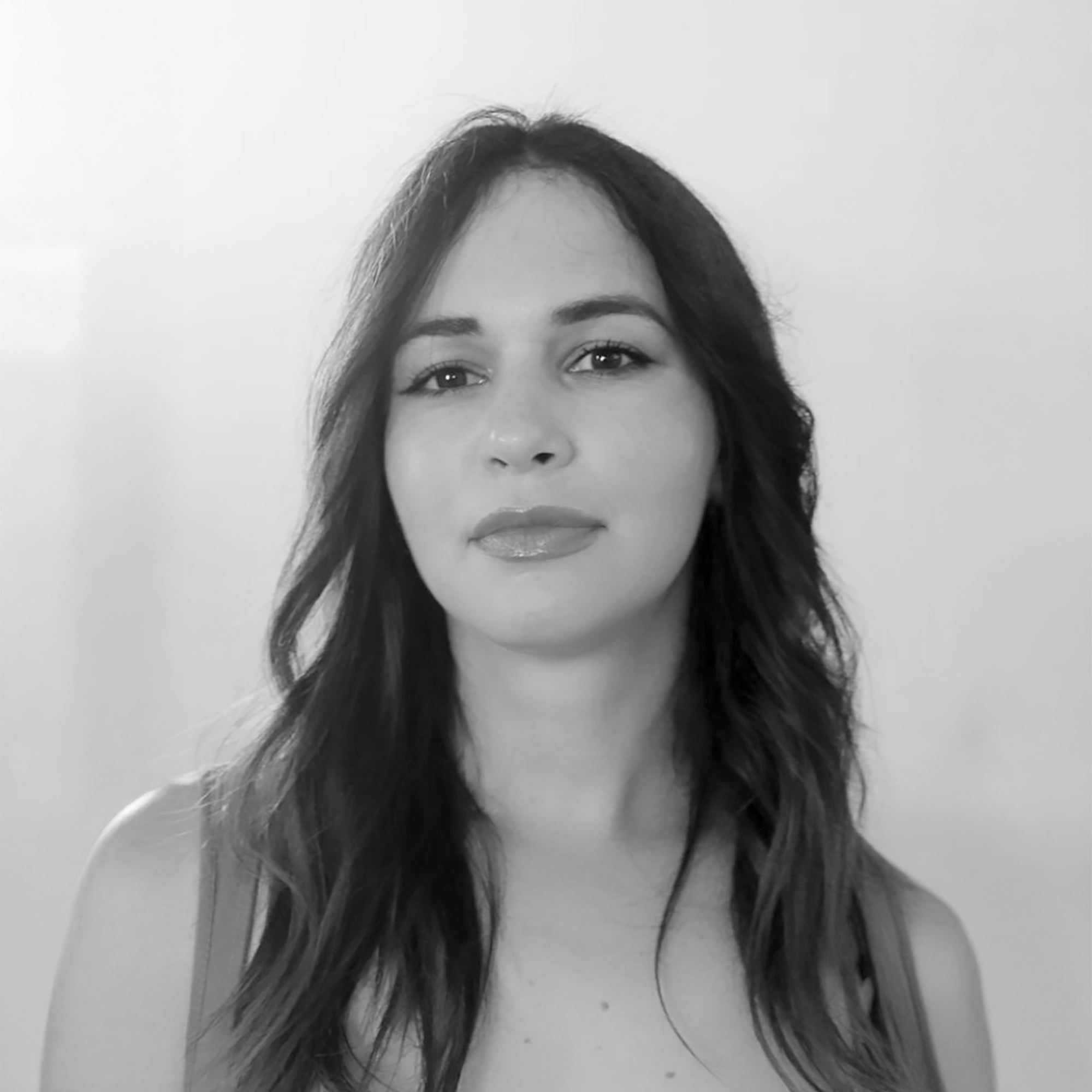 Retrato en blanco y negro de una mujer con cabello largo y oscuro, usando un top de tirantes, con expresión serena, frente a fondo claro.
