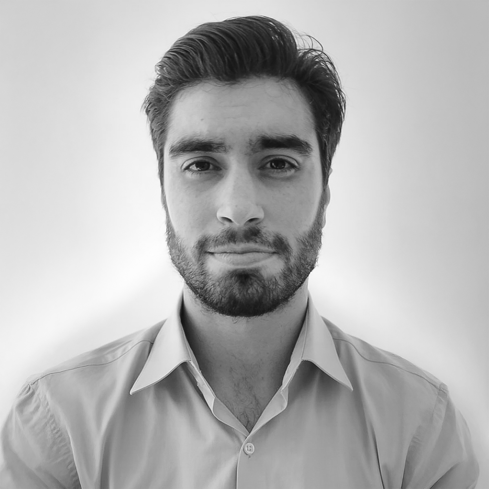 Retrato en blanco y negro de un hombre joven con barba, cabello peinado hacia atrás, usando camisa con cuello, mirando a la cámara, fondo liso claro.
