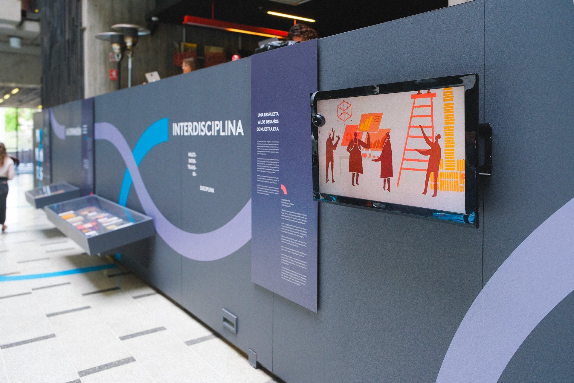 Muro «Interdisciplina» de la exposición, con una pantalla que muestra el corto.