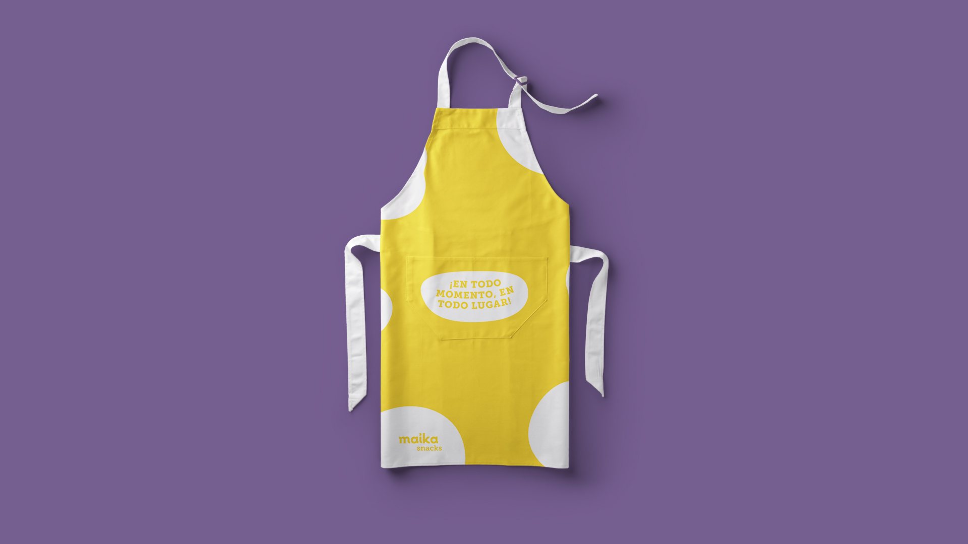 Diseño de delantal amarillo de Maika con manchas blancas, la frase «¡En todo momento, en todo lugar!» en el bolsillo y el logotipo abajo.