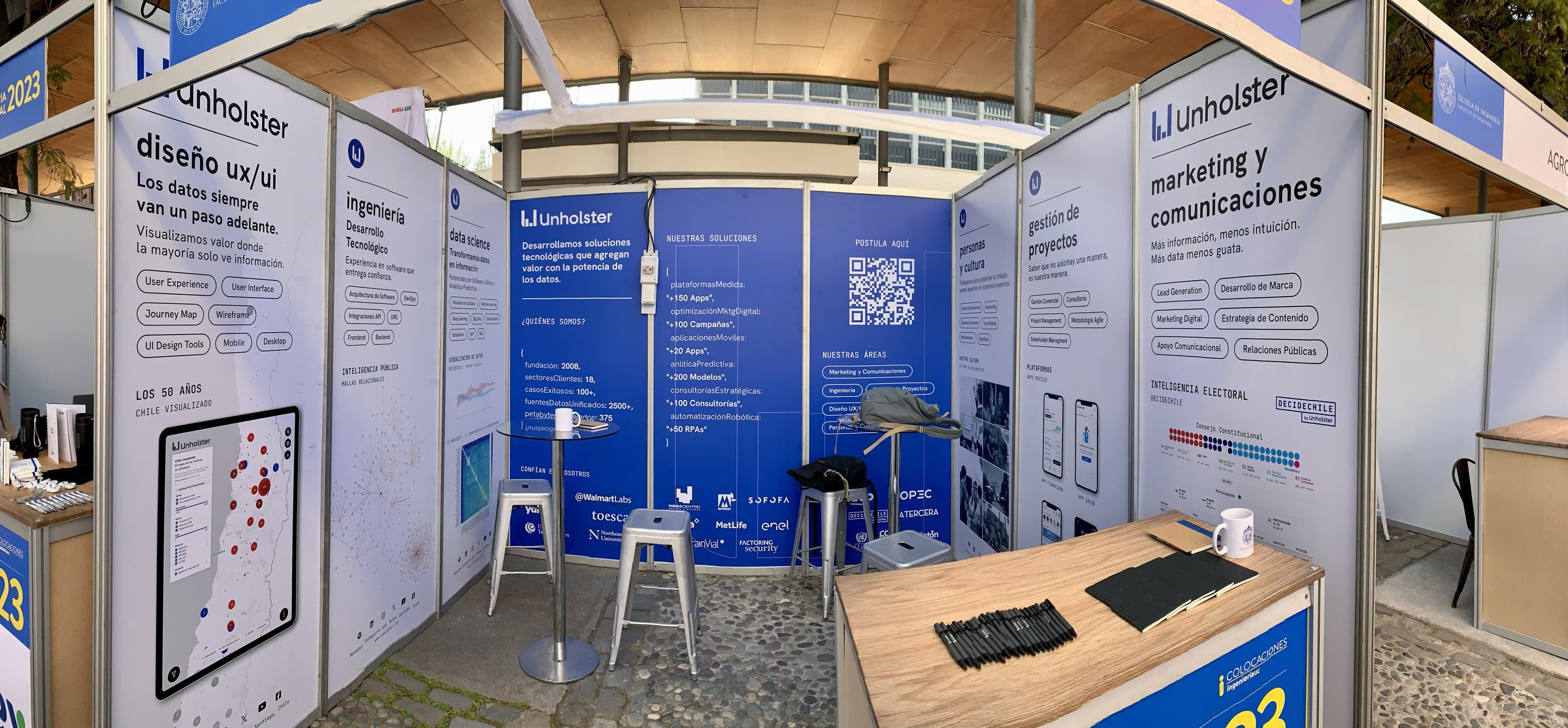 Stand de Unholster en una feria de 2023, con paneles azules y blancos por área: diseño UX/UI, ingeniería, ciencia de datos y marketing.